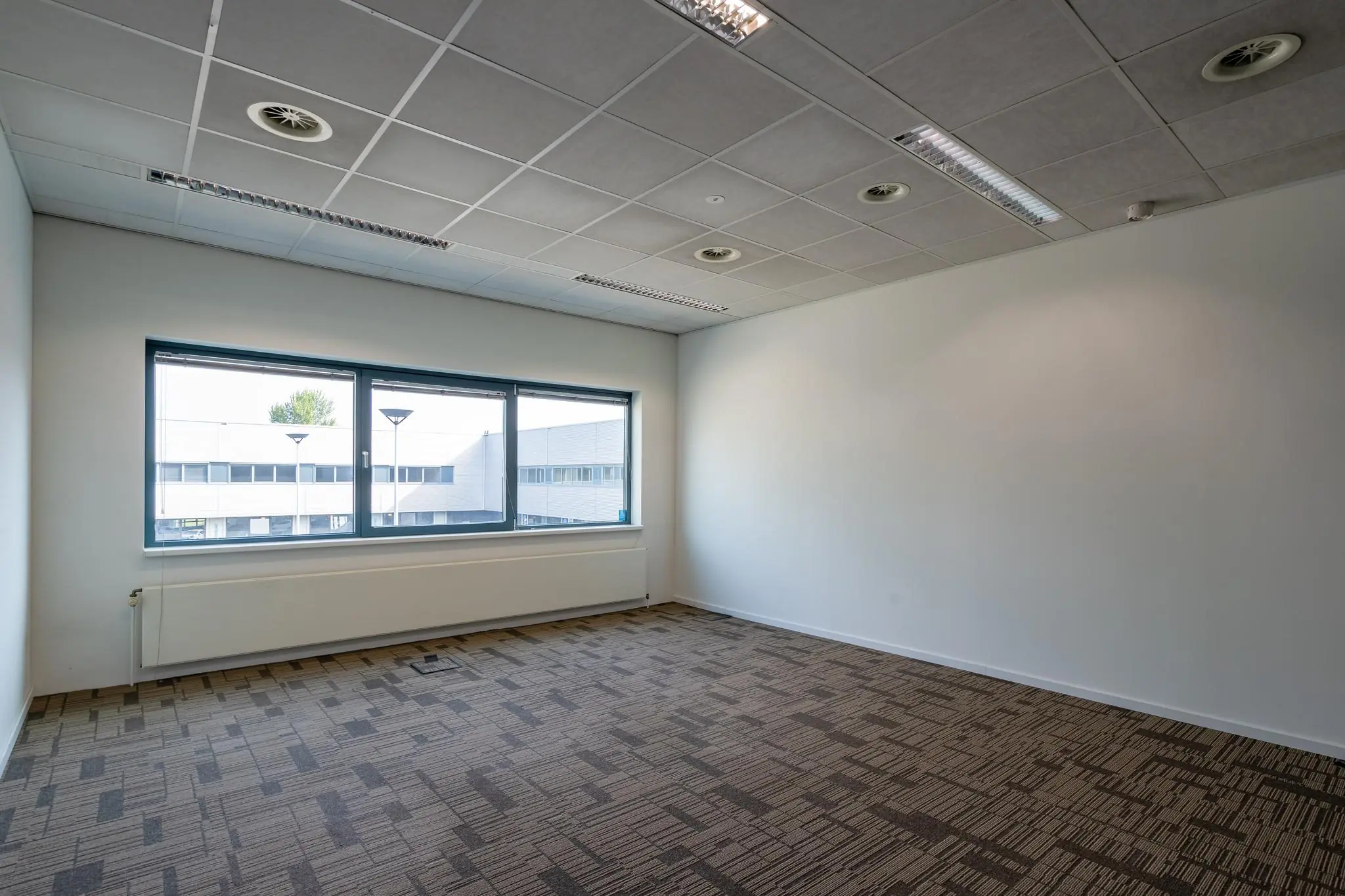 Lege kantoorruimte met tapijtvloer, systeemplafond en groot raam aan het Rivium Boulevard.